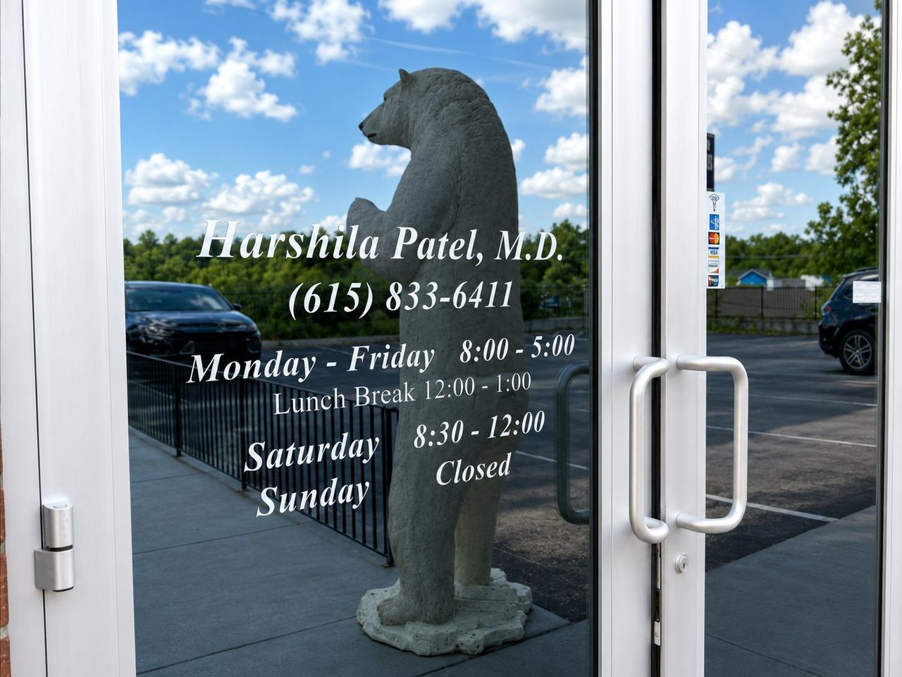 Front door signage for Harshila Patel, M.D. listing office hours beside a standing bear statue